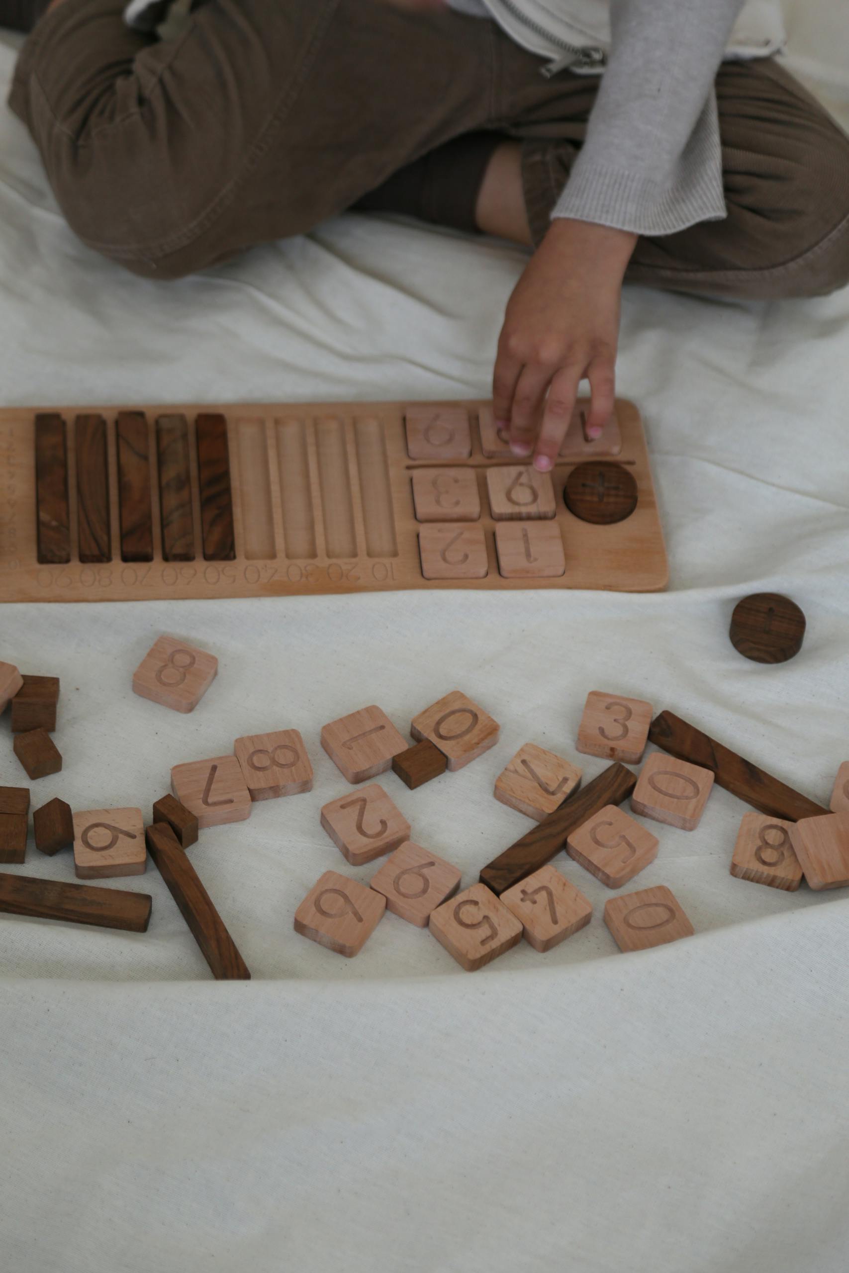 Child arranging wooden educational number blocks on a board indoors, promoting learning through play.
