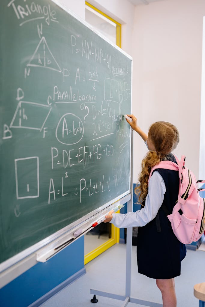 Young girl student writing math equations on classroom blackboard during a lesson.